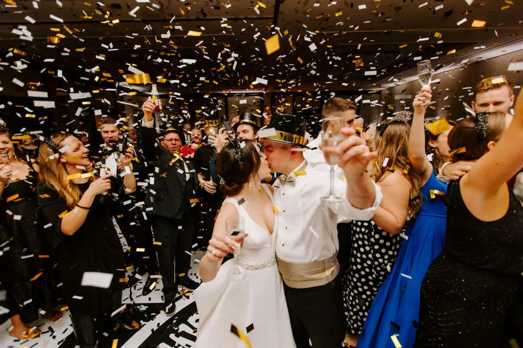 Bride and groom kissing as gold and white confetti falls at a New Year's Eve reception