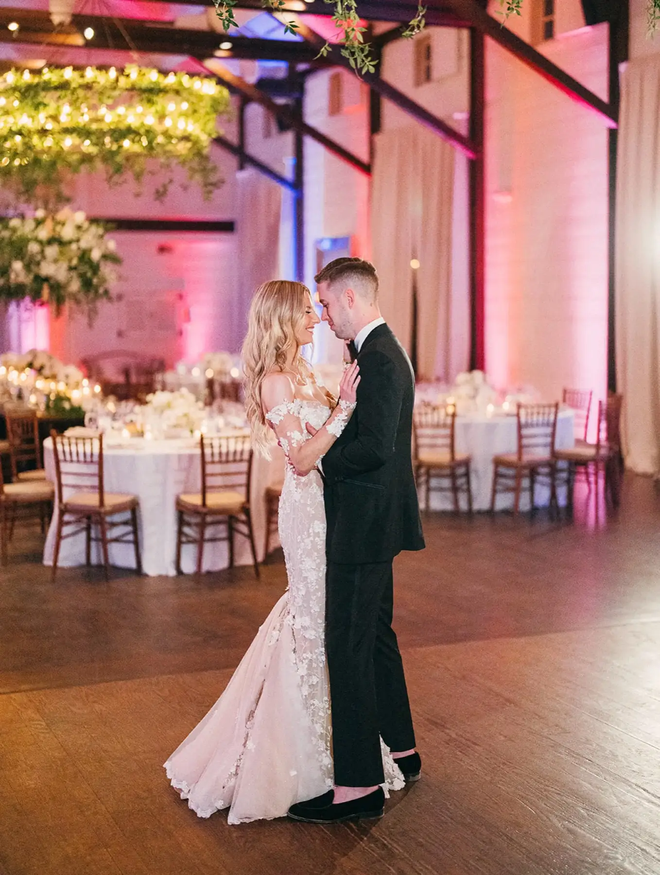 Couple sharing a dance in a ballroom washed in soft pink uplighting